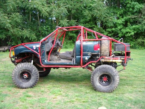 1985 Ford Bronco - This heavily modified off-road vehicle features a prominent red roll cage and oversized tires, suggesting it's built for extreme terrain.