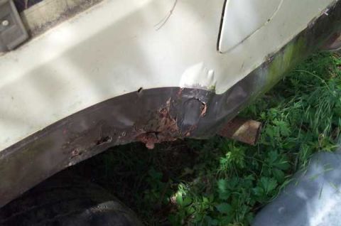 1979 Ford Bronco - Close-up of a heavily rusted lower body panel and exhaust pipe on a vehicle.