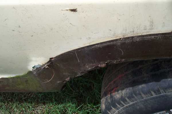 close-up of a rusted wheel well on a vehicle, showing damage and a tire