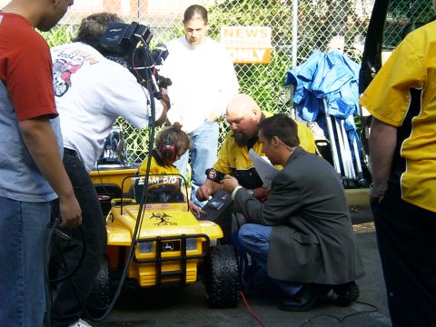 2000 Ford Excursion - A child in a toy vehicle is interviewed by a reporter, with a camera crew present.