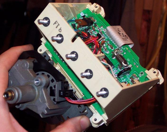 hand holding a car's electronic control module with visible circuit board and wiring