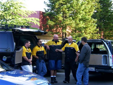 2000 Ford Excursion - Several men gather around two large SUVs, one with its rear hatch and side door open, revealing a custom interior.