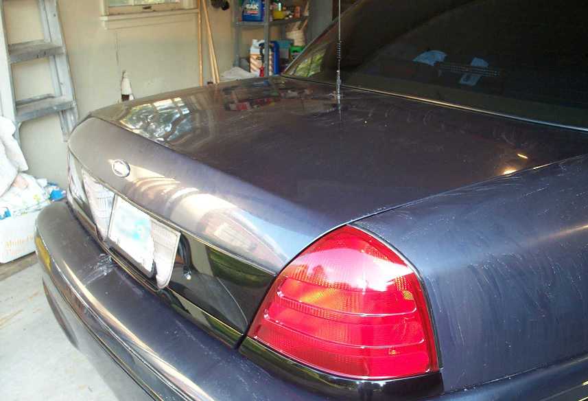 Rear of dark gray Ford Crown Victoria sedan in a garage showing trunk and taillight