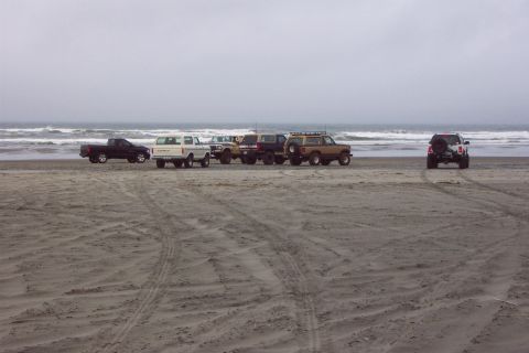 1996 Ford Bronco - Multiple vehicles, including a 1996 Ford Bronco, are parked on the beach near the ocean.