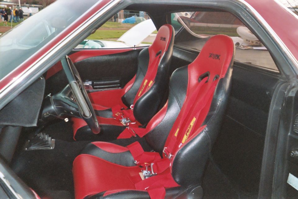 Car interior with red and black racing seats and red harnesses, steering wheel at left