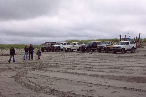 1996 Ford Bronco - A group of SUVs are parked on a sandy beach under a cloudy sky.