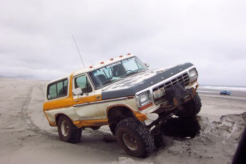1996 Ford Bronco - Modified Ford Bronco with large tires navigating a sandy beach, with another vehicle visible on the horizon.