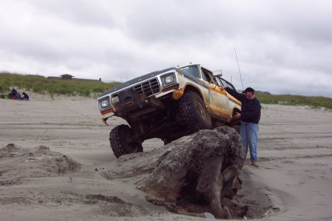 1996 Ford Bronco - A man stands by a lifted Ford F-Series truck navigating a sandy beach with large rocks.
