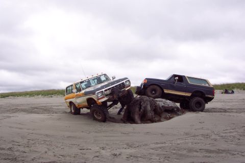 1996 Ford Bronco - Two off-road vehicles navigate a sandy beach, with one appearing to be a 1978 Ford Bronco.