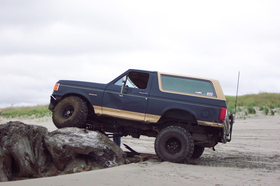 Lifted blue and tan Ford Bronco climbing driftwood log on a beach