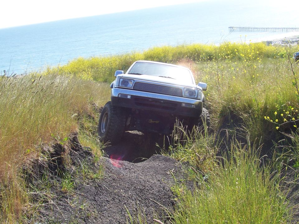 Lifted Toyota truck articulating a front wheel in a rut on a coastal hillside