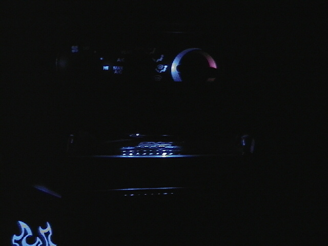 Car interior at night with glowing blue and red lights on the dashboard and a flame decal on the door