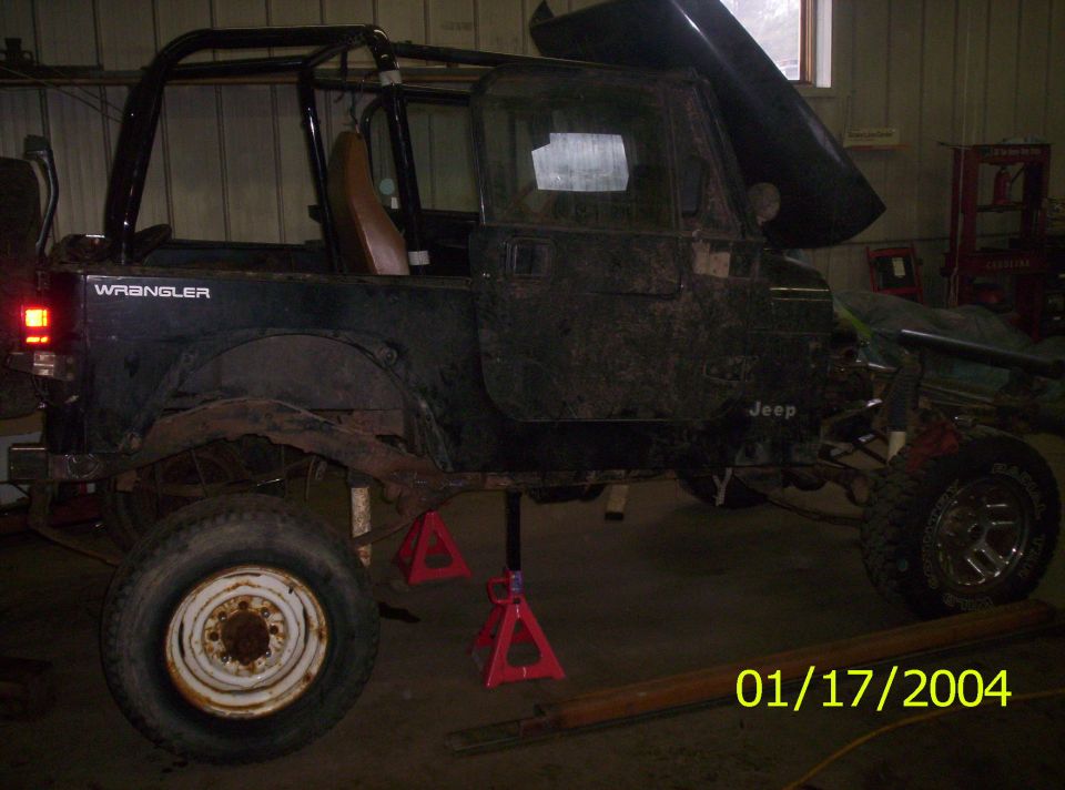 Black Jeep Wrangler on red jack stands in a garage, hood raised and one wheel removed