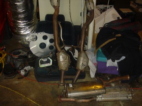 1986 Ford Mustang - Several exhaust system components are laid out on the floor, alongside a car seat and other miscellaneous items.