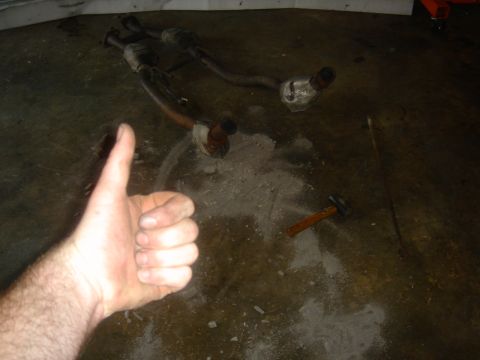1986 Ford Mustang - Exhaust pipes and a hammer are on the floor, possibly after a repair or before a repair.