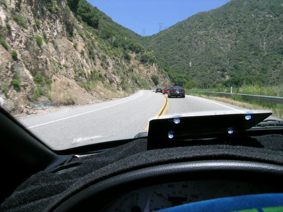 Interior view of car dashboard and windshield looking out at a winding mountain road with several cars ahead