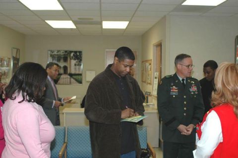 1996 Ford Probe - Denzel Washington is seen signing a document in an indoor setting, surrounded by several individuals.