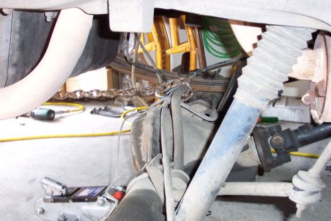 1992 Ford Bronco - Underbody view of a 4x4 front suspension and driveline, with a rusty roller chain looped around a leaf spring and axle housing as a makeshi…
