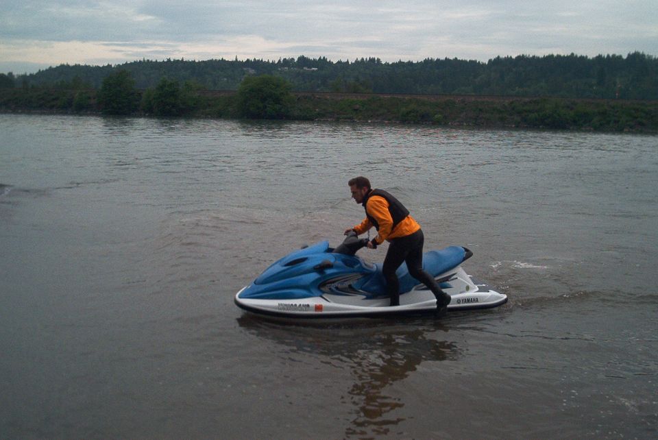 Man standing on a blue and white Yamaha jet ski on a calm river