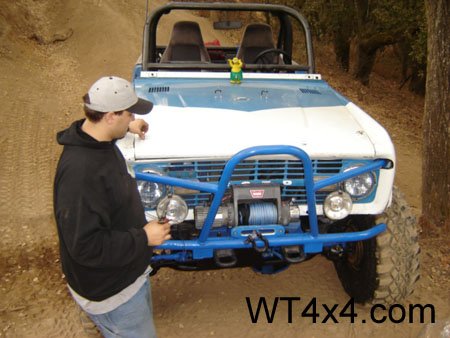 1971 Ford Bronco - A man stands next to a 1971 Ford Bronco modified for off-road use, a blue brush guard and winch.