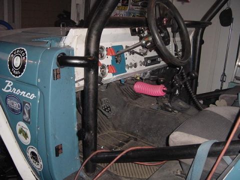1971 Ford Bronco - The interior of a modified off-road vehicle shows a roll cage, custom dash, and stickers on the driver's side door.