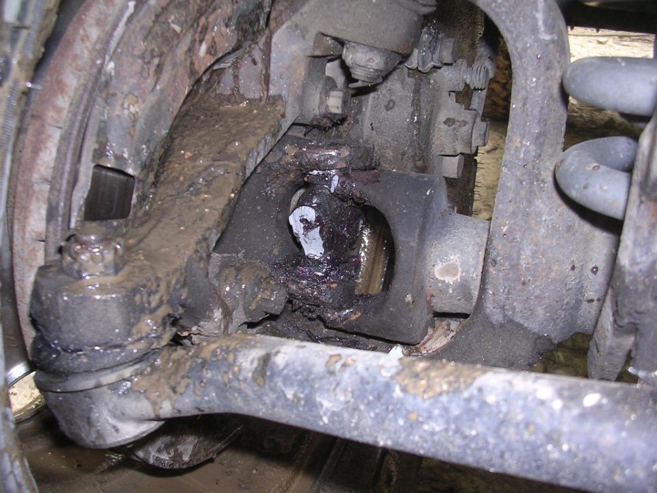 Muddy, grease-covered front steering knuckle and axle joint on a Jeep Cherokee suspension