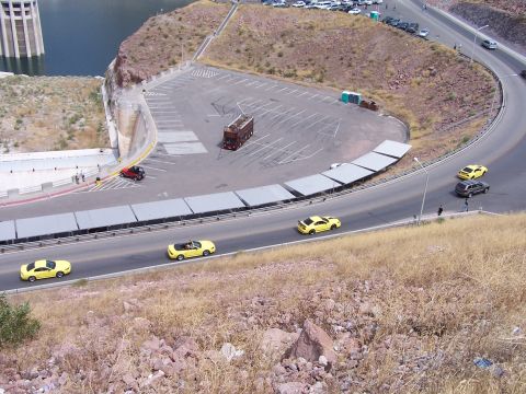 2002 Ford GT - A yellow convertible sports car is seen driving on a road with other vehicles near a large dam structure.