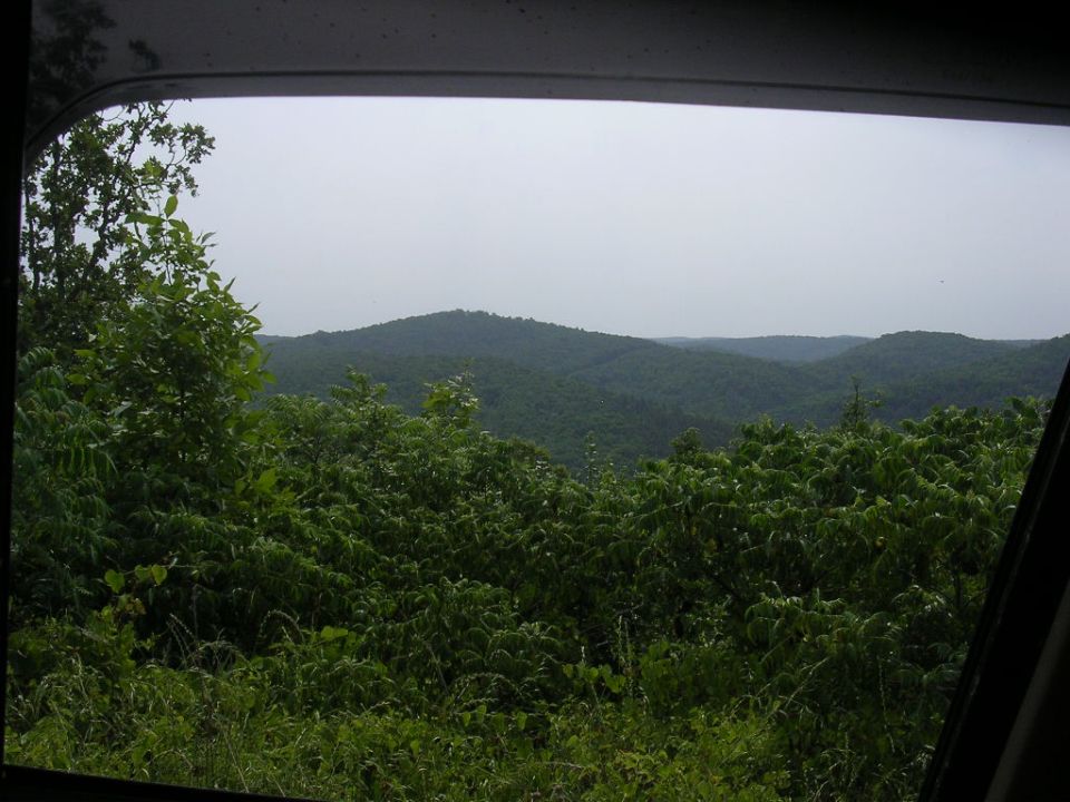 View of green forested hills through a car window, with a Supermotors watermark