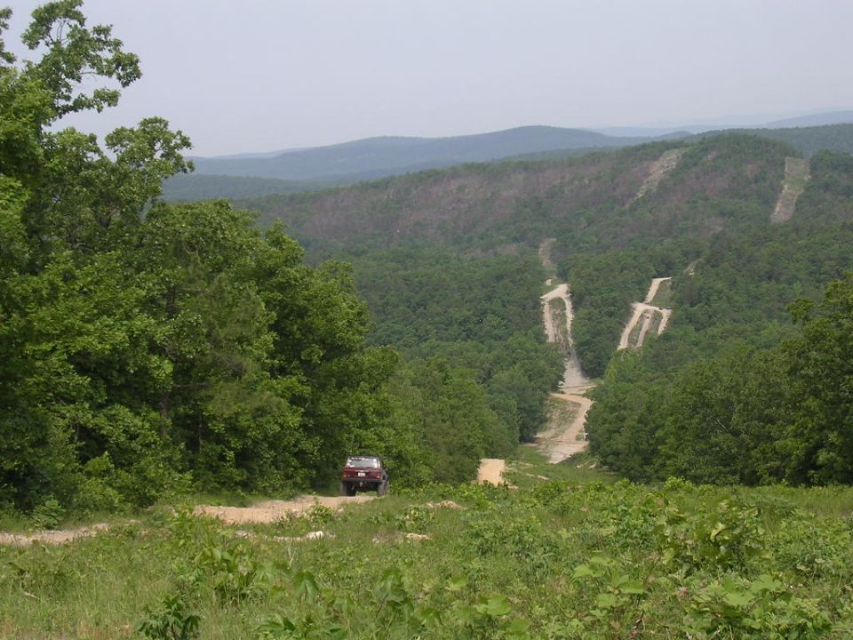 Red 1995 Jeep Cherokee from rear on dirt road with wooded hills