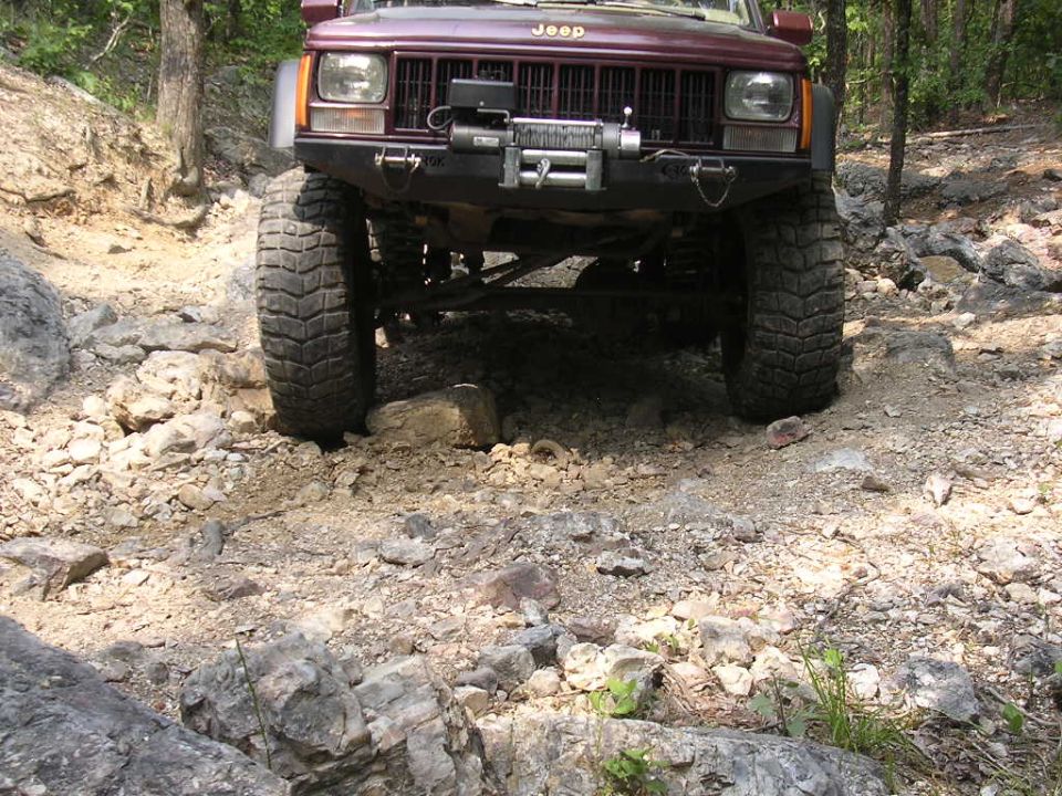 Front view of a 1995 Jeep Cherokee on a rocky trail, with a winch mounted on the bumper