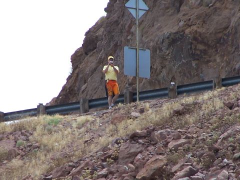 2002 Ford GT - A person stands on a rocky slope, holding a camera up to take a picture near a road.