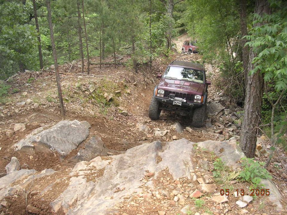 Maroon 1995 Jeep Cherokee on a rocky off-road trail with another vehicle behind