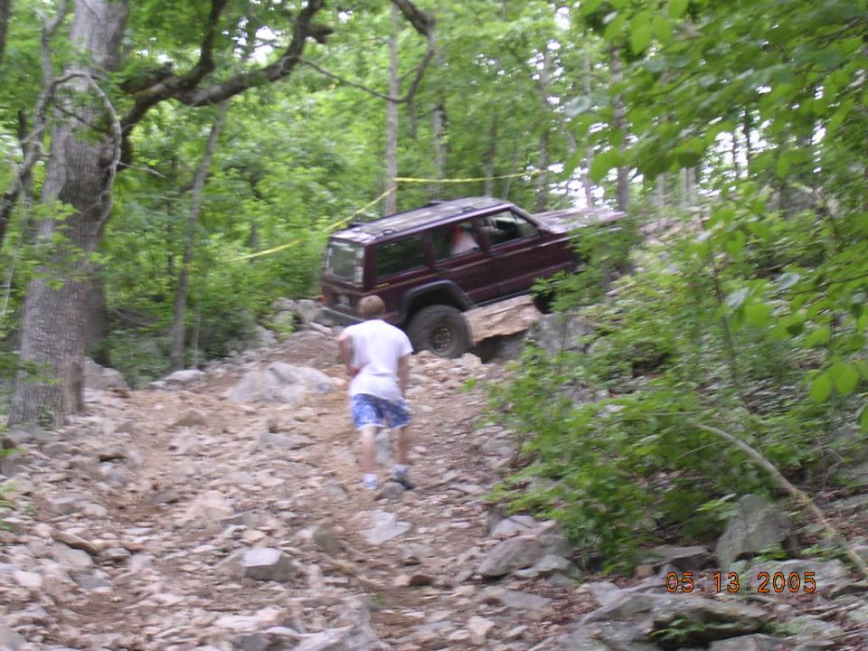 Maroon 1995 Jeep Cherokee climbing a rocky hill with a person walking behind it