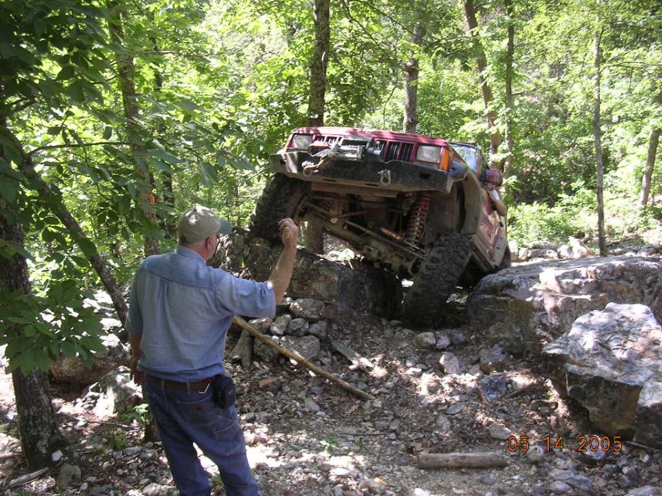 1995 Jeep Cherokee climbing large rocks on a wooded trail, driver giving directions