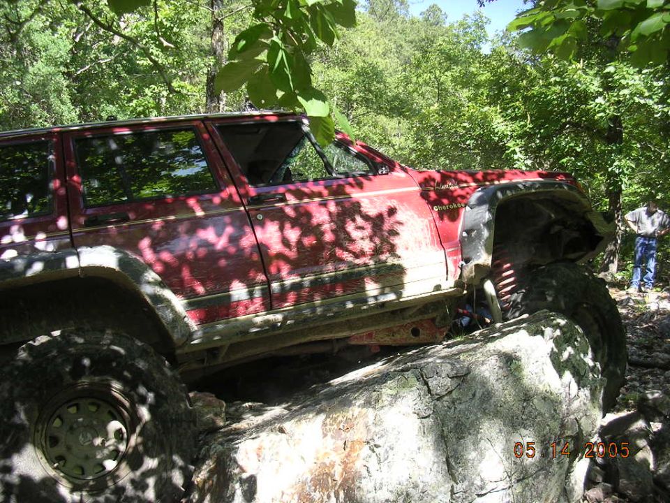 Red 1995 Jeep Cherokee off-roading over large rocks