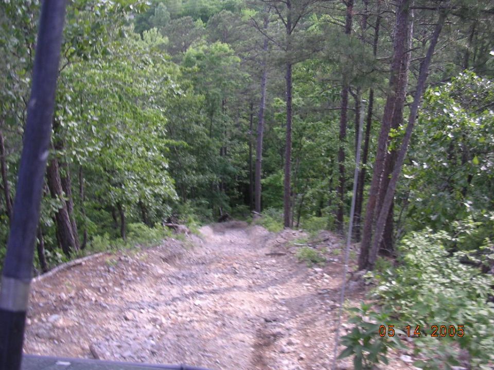 Dirt trail going downhill through a forest, with trees on both sides. A date stamp reads 05/14/2005