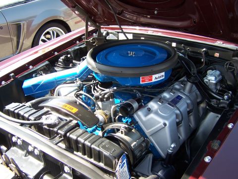 2002 Ford GT - The engine bay of a 1969 Ford Mustang features a prominent blue air cleaner and intake system, with another Mustang visible in the backgrou…