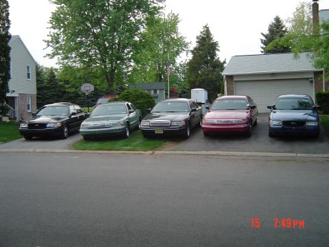 1999 Ford Crown Victoria - Multiple Ford Crown Victoria sedans are parked in a residential driveway, displaying various colors and model years.