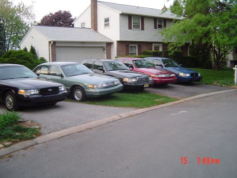 1999 Ford Crown Victoria - A row of four Ford Crown Victoria sedans, all appearing to be from the 1999 model year, are parked in a residential driveway.
