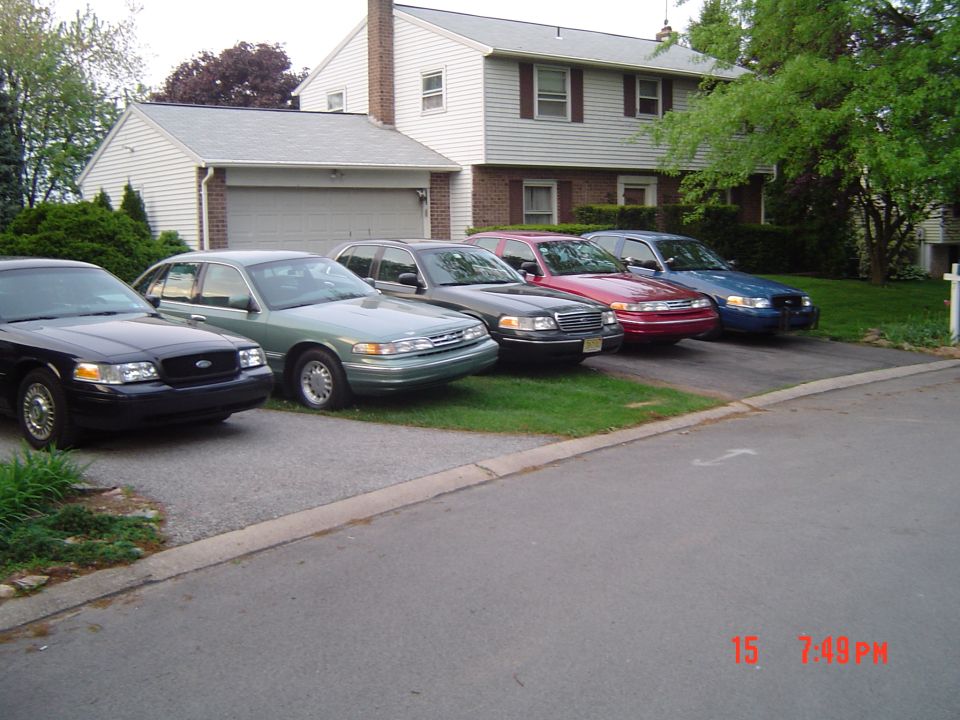 Four 1999 Ford Crown Victoria sedans parked in a driveway, front view
