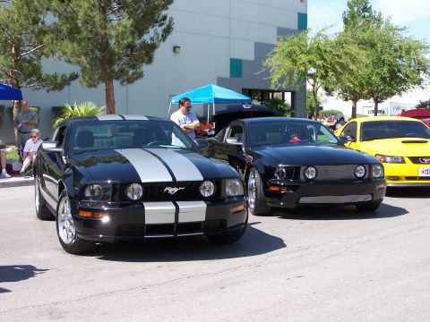 2002 Ford GT - Three Ford Mustangs are parked in a lot with people and tents in the background.