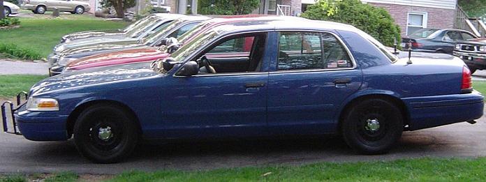Side view of a blue 1999 Ford Crown Victoria with a push bumper and black wheels