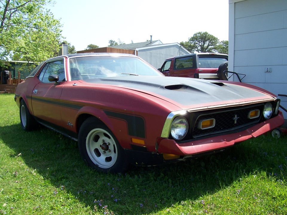 Red 1971 Ford Mustang coupe with black hood scoop and racing stripes parked on grass
