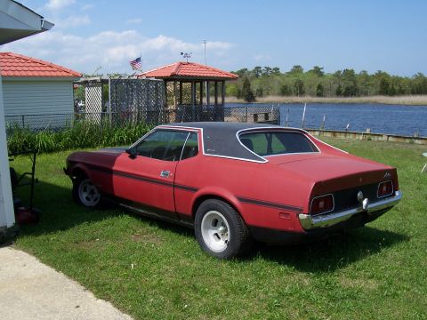 1971 Ford Mustang - A red coupe with a black vinyl roof sits on a grassy lawn next to a body of water.
