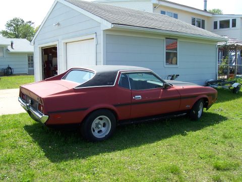 1971 Ford Mustang - This 1971 Ford Mustang coupe features a distinctive black vinyl top and is seen parked in a grassy yard next to a garage.