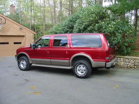 2002 Ford Excursion - A red 2002 Ford Excursion is parked in a driveway with a garage and trees in the background.