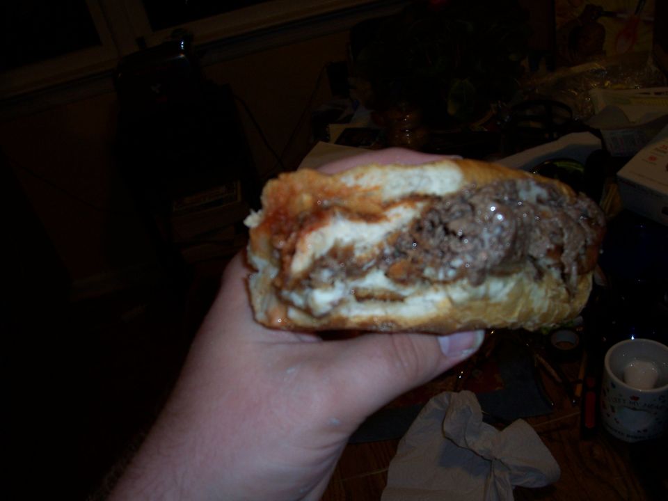 Hand holding a large sandwich with meat and sauce