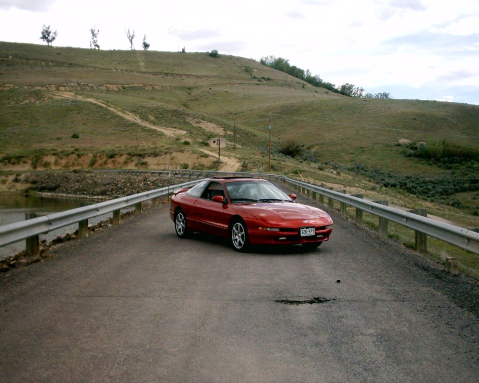 Red 1996 Ford Probe coupe on a road with a scenic hill background