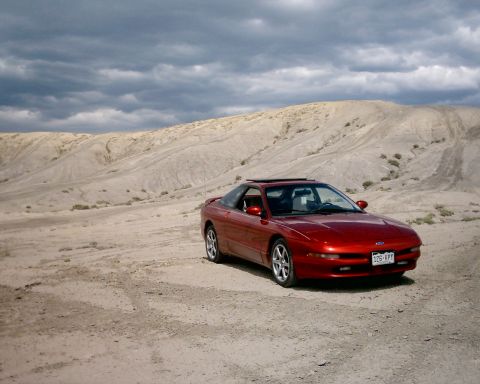 1996 Ford Probe - A red 1996 Ford Probe sits in a dry, dusty landscape under a cloudy sky.