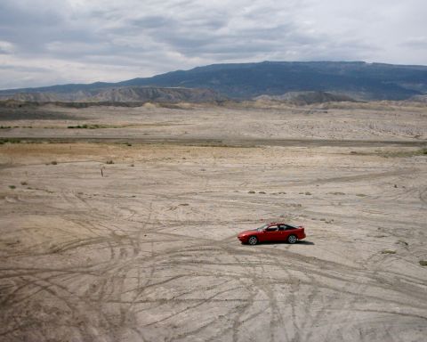 1996 Ford Probe - A red 1996 Ford Probe is parked in a barren, dusty landscape with tire tracks visible on the ground.
